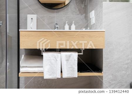 A sleek wooden bathroom vanity with white sink, modern mirror, and neatly arranged fresh towels, reflecting contemporary interior design and upscale hospitality A sleek wooden bathroom vanity with white sink, modern mirror, and neatly arranged fresh towels, reflecting contemporary interior design and upscale hospitality 139412440