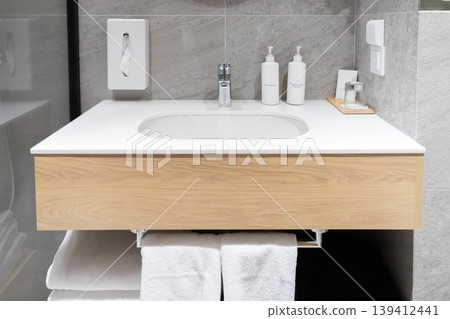 Clean, modern hotel bathroom interior featuring a wooden vanity, white sink, personal care products, and fresh towels, emphasizing hygiene and guest comfort 139412441