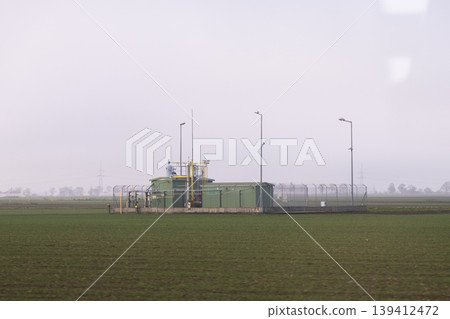 Green natural gas station with interconnected pipelines securely fenced in a wide, misty field, symbolizing essential energy infrastructure for industrial power Green natural gas station with interconnected pipelines securely fenced in a wide, misty field, symbolizing essential energy infrastructure for industrial power 139412472