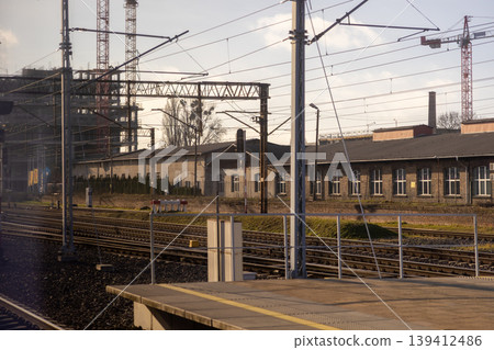 Railway tracks and empty platform with industrial buildings and large construction cranes, signifying urban development and growth 139412486