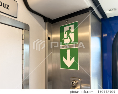 Essential green emergency exit symbols and a downward arrow sign on a metal panel inside public transport, providing vital safety guidance for quick passenger evacuation Essential green emergency exit symbols and a downward arrow sign on a metal panel inside public transport, providing vital safety guidance for quick passenger evacuation 139412505
