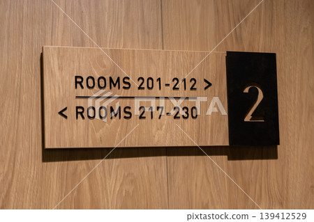 Modern wooden hotel floor sign displays room numbers 201-212 and 217-230, providing clear direction for guests in a contemporary hospitality setting Modern wooden hotel floor sign displays room numbers 201-212 and 217-230, providing clear direction for guests in a contemporary hospitality setting 139412529