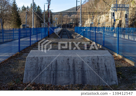 A remote railway track extends through a natural mountain landscape, protected by vibrant blue fences, symbolizing travel, connection, and robust transportation infrastructure A remote railway track extends through a natural mountain landscape, protected by vibrant blue fences, symbolizing travel, connection, and robust transportation infrastructure 139412547