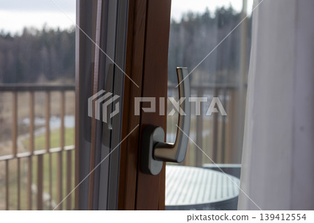 Modern wooden window frame featuring a sleek metallic handle, providing a serene outdoor balcony view of lush nature, perfect for a cozy home or hotel Modern wooden window frame featuring a sleek metallic handle, providing a serene outdoor balcony view of lush nature, perfect for a cozy home or hotel 139412554