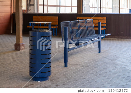 Blue metal public bench and trash can in an empty transport waiting area, symbolizing urban utility, travel, and quiet service 139412572