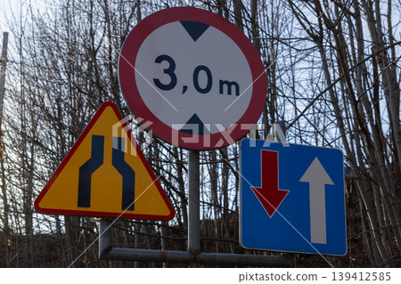 Road signs on a pole display a 3,0 m height limit, road narrowing, and traffic priority, guiding driver safety and efficient urban navigation Road signs on a pole display a 3,0 m height limit, road narrowing, and traffic priority, guiding driver safety and efficient urban navigation 139412585