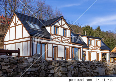 Modern half-timbered houses with white facades and dark roofs, set against a mountainous landscape, capturing rustic charm for real estate or vacation 139412640