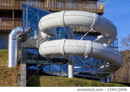 Prominent white water slide tubes and sleek metallic ventilation pipes emerge from a contemporary resort building, promising thrilling outdoor leisure and memorable holiday recreation Prominent white water slide tubes and sleek metallic ventilation pipes emerge from a contemporary resort building, promising thrilling outdoor leisure and memorable holiday recreation 139412646