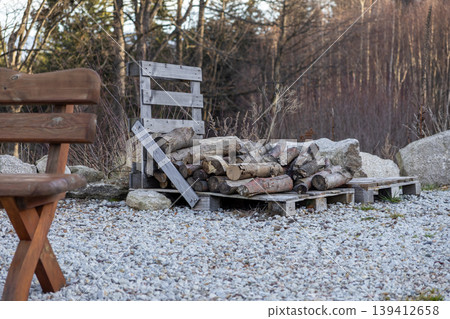 Rustic stacked firewood logs on wooden pallets with a cozy bench on gravel, symbolizing natural warmth and sustainable energy for home 139412658
