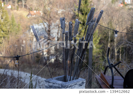 Wooden-handled metal skewers stand weathered in a gray stone planter, creating a cozy atmosphere for outdoor cooking and barbecue gatherings during autumn 139412662