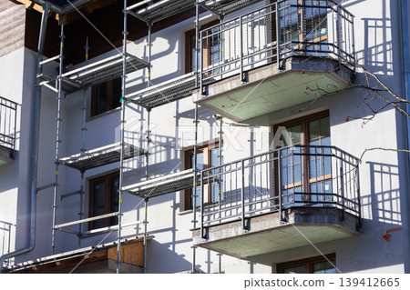 Urban residential building undergoing renovation, covered in sturdy metal scaffolding, showcasing balconies and windows, symbolizing construction, repair, and housing progress Urban residential building undergoing renovation, covered in sturdy metal scaffolding, showcasing balconies and windows, symbolizing construction, repair, and housing progress 139412665