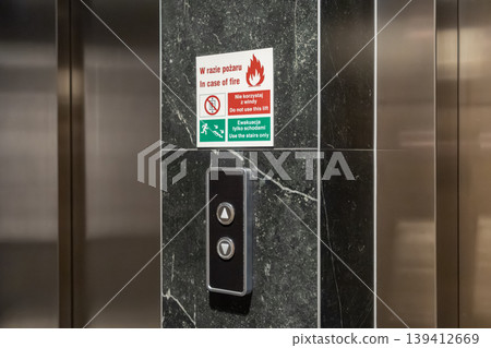 Elevator call buttons on marble, displaying a crucial fire safety sign stating In case of fire, use stairs only, emphasizing building evacuation procedure 139412669