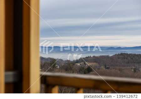 Serene panoramic misty mountain landscape featuring layered blue hills and bare forest trees, framed by a rustic wooden balcony, embodying peaceful nature scenery Serene panoramic misty mountain landscape featuring layered blue hills and bare forest trees, framed by a rustic wooden balcony, embodying peaceful nature scenery 139412672