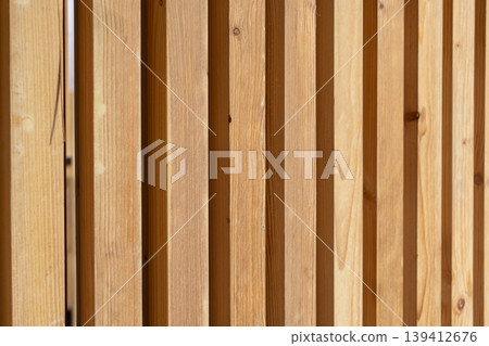 Warm wooden slat wall texture featuring parallel vertical planks, providing a natural aesthetic background for modern architectural design and construction concepts 139412676