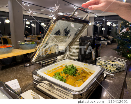 Hand opening a food warmer lid showcasing hot chicken wings buffet service in a hotel restaurant, perfect for holiday dining 139412691