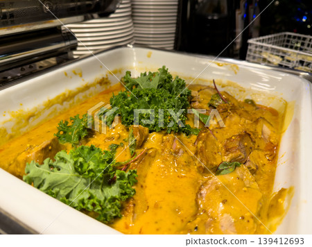 Buffet dish featuring savory curry with tender meat in a rich yellow sauce, garnished with fresh kale, perfect for catering and festive events Buffet dish featuring savory curry with tender meat in a rich yellow sauce, garnished with fresh kale, perfect for catering and festive events 139412693