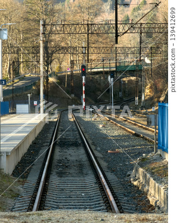 Railway station platform view with diverging train tracks, overhead lines, and a red signal, representing essential infrastructure for transport and travel Railway station platform view with diverging train tracks, overhead lines, and a red signal, representing essential infrastructure for transport and travel 139412699
