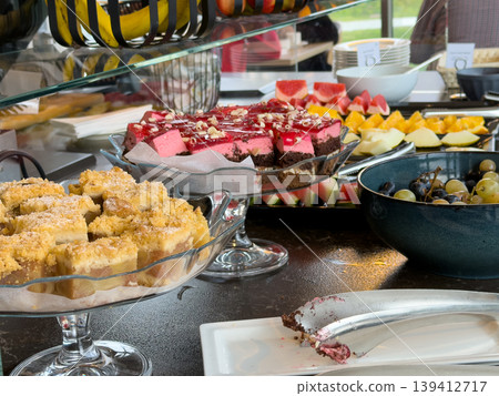 Appetizing buffet offering varied sweet desserts, including delicious crumb cake and vibrant mousse, with fresh fruit, ideal for hotel breakfast or event catering Appetizing buffet offering varied sweet desserts, including delicious crumb cake and vibrant mousse, with fresh fruit, ideal for hotel breakfast or event catering 139412717