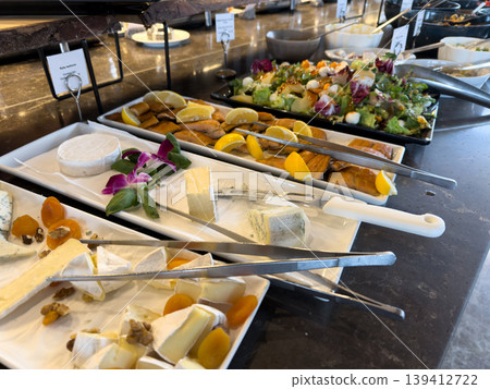 Diverse buffet selection with fresh cheese varieties, smoked salmon, and a vibrant mixed salad, offering healthy gourmet options for hotel guests 139412722