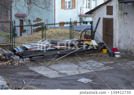 Untidy backyard scene with an old shed and a large pile of discarded construction materials, representing neglect and environmental concerns in a rural setting 139412730