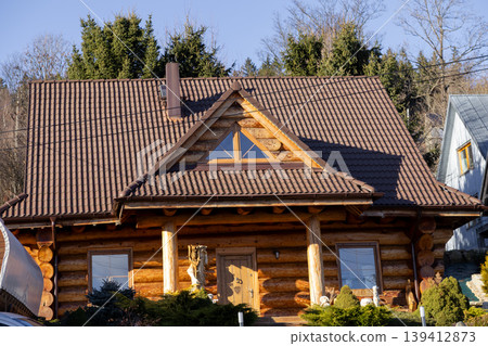 Rustic wooden log cabin house with a brown tiled roof and triangular window, surrounded by green trees, offering a peaceful and natural living environment Rustic wooden log cabin house with a brown tiled roof and triangular window, surrounded by green trees, offering a peaceful and natural living environment 139412873