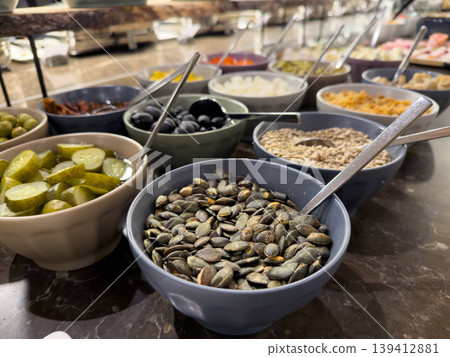 Buffet bar featuring various bowls of healthy seeds, olives, and pickles, offering diverse nutritious options for a hotel breakfast or salad 139412881