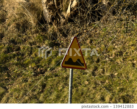 Yellow triangular road sign clearly indicates an uneven road surface, providing essential warning for drivers about potential bumps ahead in a natural rural outdoor setting Yellow triangular road sign clearly indicates an uneven road surface, providing essential warning for drivers about potential bumps ahead in a natural rural outdoor setting 139412883