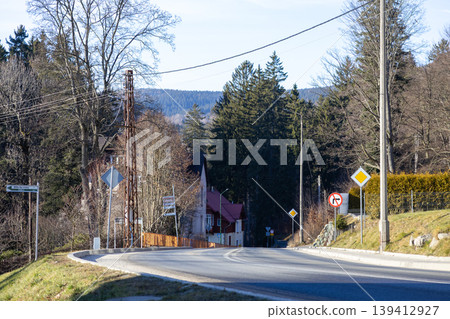 Winding paved road curving through a scenic mountainous village landscape with bare and evergreen trees under a clear sky, depicting a peaceful journey Winding paved road curving through a scenic mountainous village landscape with bare and evergreen trees under a clear sky, depicting a peaceful journey 139412927