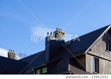 Dark metal roof and wooden wall of house, with two chimneys, metal vents under blue sky, for modern building and construction 139412931