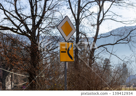 Yellow diamond priority road sign and junction diagram on a pole, conveying essential traffic rules for safe driving and navigation Yellow diamond priority road sign and junction diagram on a pole, conveying essential traffic rules for safe driving and navigation 139412934