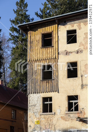 Abandoned multi-story building facade with weathered wooden planks, broken windows, peeling plaster, symbolizing urban decay and renewal 139412971