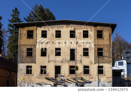 Old dilapidated urban building displaying peeling facade, empty windows, and weathered wooden cladding, symbolizing decay, neglect, and regeneration Old dilapidated urban building displaying peeling facade, empty windows, and weathered wooden cladding, symbolizing decay, neglect, and regeneration 139412973