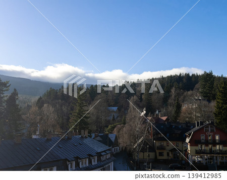 Scenic view of a picturesque European mountain village with traditional buildings nestled in a forest valley, under a clear blue sky, evoking serene travel 139412985