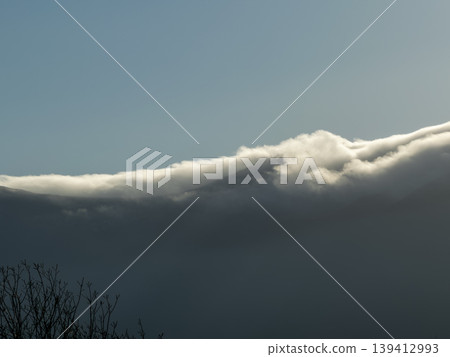 Sunlit horizontal cloud layer creates dramatic contrast above dark, stormy weather under clear sky, showcasing nature's powerful atmospheric changes 139412993