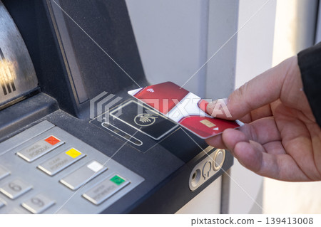 Person's hand inserting a red contactless banking card into an outdoor ATM terminal, facilitating secure financial transactions and cash withdrawals Person's hand inserting a red contactless banking card into an outdoor ATM terminal, facilitating secure financial transactions and cash withdrawals 139413008