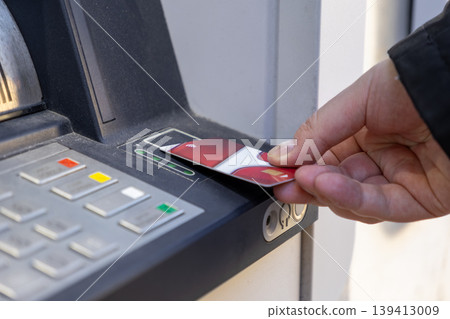 Person inserting a red payment card into an automatic teller machine, performing a secure financial transaction for modern banking services Person inserting a red payment card into an automatic teller machine, performing a secure financial transaction for modern banking services 139413009