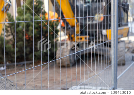 Temporary metal fence provides safety, with a blurred excavator working on a construction site, symbolizing urban development and progress 139413010