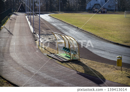 Empty athletic running track and green dugout bench on a sunny field, signifying preparation for sports, physical education, and outdoor training activities Empty athletic running track and green dugout bench on a sunny field, signifying preparation for sports, physical education, and outdoor training activities 139413014