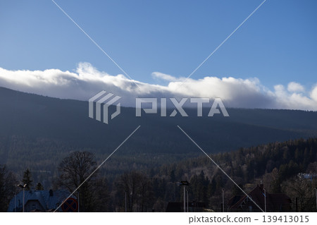 Expansive mountain range blanketed by dense green forest, topped with a dramatic line of white clouds against a vibrant blue sky, evoking serene nature Expansive mountain range blanketed by dense green forest, topped with a dramatic line of white clouds against a vibrant blue sky, evoking serene nature 139413015