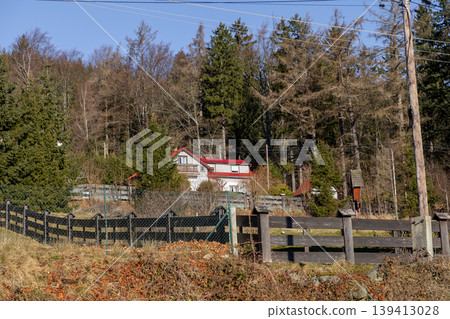 White house with a vibrant red roof nestled in a wooded hillside, portraying serene rural living and the tranquil beauty of an autumn landscape White house with a vibrant red roof nestled in a wooded hillside, portraying serene rural living and the tranquil beauty of an autumn landscape 139413028