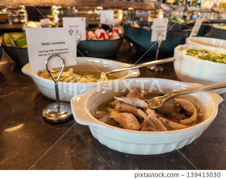 Herring with cranberries in a white bowl, served on a buffet table, offering a delicious traditional European appetizer selection for guests 139413030