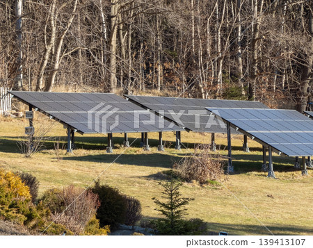 A ground mounted solar panel array sits on a grassy field near a forest, illustrating renewable energy generation, environmental sustainability, and the transition toward green power in rural settings A ground mounted solar panel array sits on a grassy field near a forest, illustrating renewable energy generation, environmental sustainability, and the transition toward green power in rural settings 139413107
