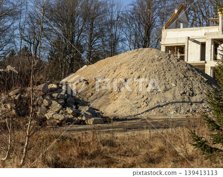 A large mound of sand and a pile of rough stones sit at an active residential construction site, representing essential urban development progress, building industry foundation, and material supply A large mound of sand and a pile of rough stones sit at an active residential construction site, representing essential urban development progress, building industry foundation, and material supply 139413113