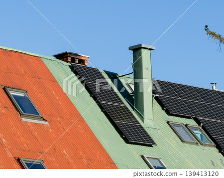 Solar panels are installed on a vibrant green and orange corrugated metal residential roof to promote sustainable energy solutions, renewable power generation, and modern eco-friendly living today 139413120