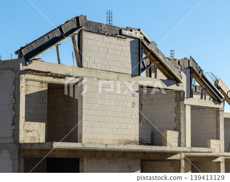 Unfinished residential building with concrete block walls and roof framing under clear blue sky, illustrating the process of real estate development and modern architectural construction site progress 139413129