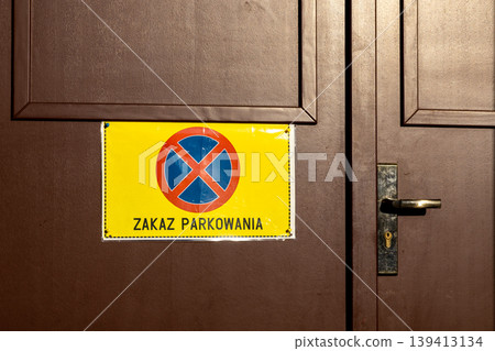 A no parking sign on a brown wooden door communicates access restrictions and warns drivers to keep the area clear in a public urban setting, emphasizing private property and clear passage rules A no parking sign on a brown wooden door communicates access restrictions and warns drivers to keep the area clear in a public urban setting, emphasizing private property and clear passage rules 139413134