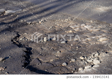 Damaged asphalt road with deep pothole and exposed cobblestone base, highlighting infrastructure decay and the urgent need for municipal street maintenance, urban repair, and public safety improvement Damaged asphalt road with deep pothole and exposed cobblestone base, highlighting infrastructure decay and the urgent need for municipal street maintenance, urban repair, and public safety improvement 139413141