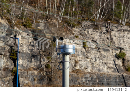Anemometer measuring wind speed and direction on a metal post, set against a rocky mountain slope to emphasize meteorological monitoring, environmental research, and weather data collection technology Anemometer measuring wind speed and direction on a metal post, set against a rocky mountain slope to emphasize meteorological monitoring, environmental research, and weather data collection technology 139413142