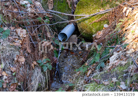 A plastic drainage pipe discharges clear water into a mountain stream, illustrating essential water management infrastructure and sustainable resource conservation within a lush, wild forest landscape A plastic drainage pipe discharges clear water into a mountain stream, illustrating essential water management infrastructure and sustainable resource conservation within a lush, wild forest landscape 139413159