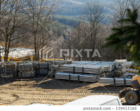 Stacked metal scaffolding poles at a construction site reflect ongoing industrial development and infrastructure growth in a rural forest area with heavy machinery present during the daily operation 139413168